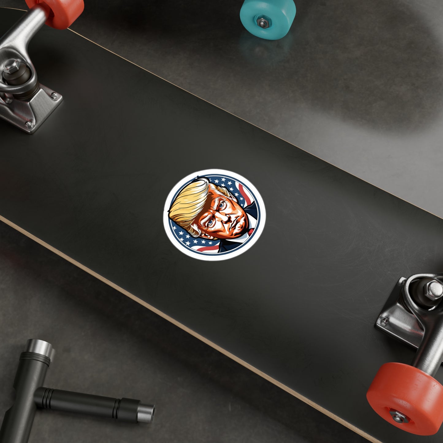 Round sticker featuring a bold, graphic illustration of a determined figure with distinctive golden hair. The background showcases stars and stripes, symbolizing the American flag, adding a patriotic theme to the design displayed on a skate board