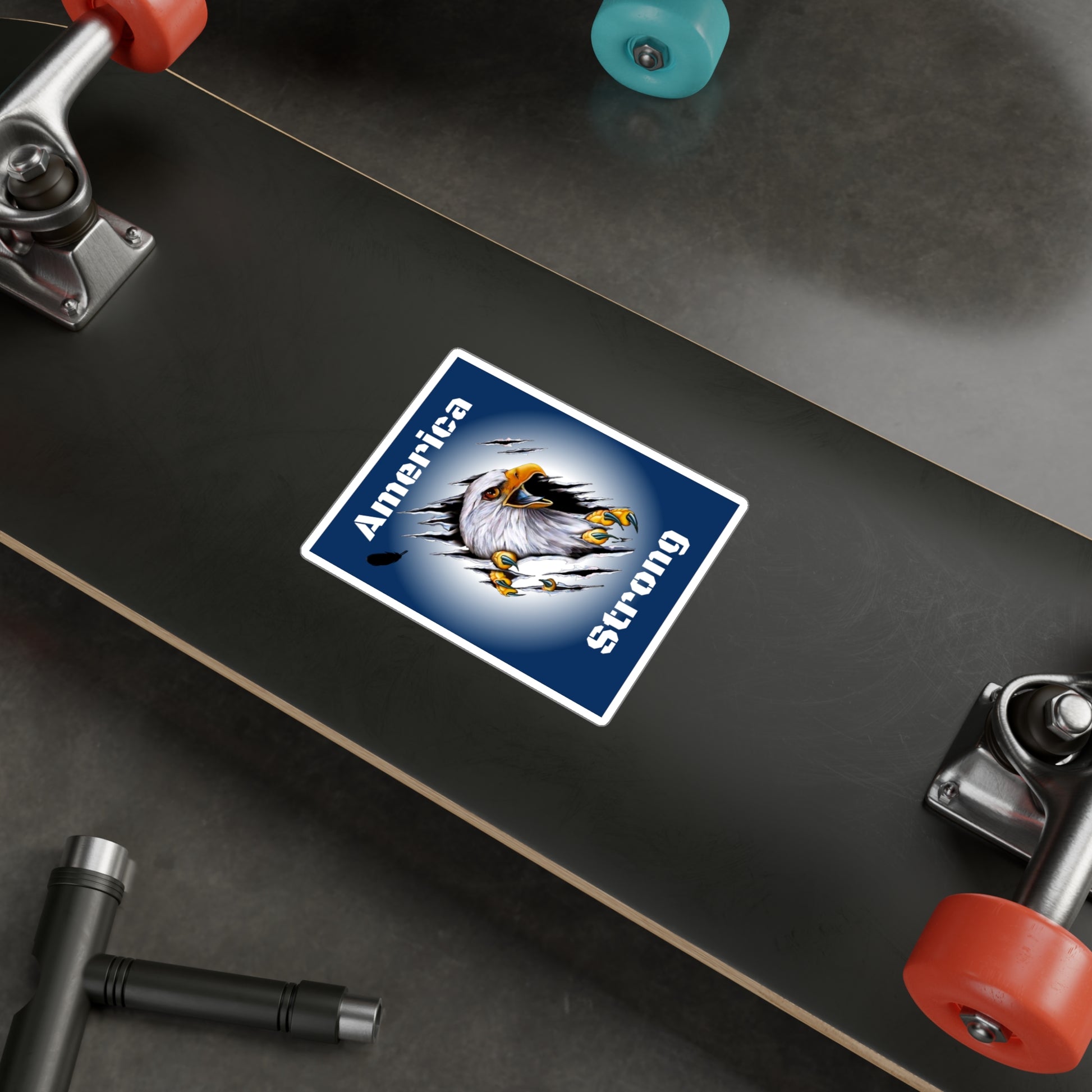 Blue decal showing an eagle ripping through the middle of the design with the words, "America Strong", around the eagle being displayed on a skate board. 