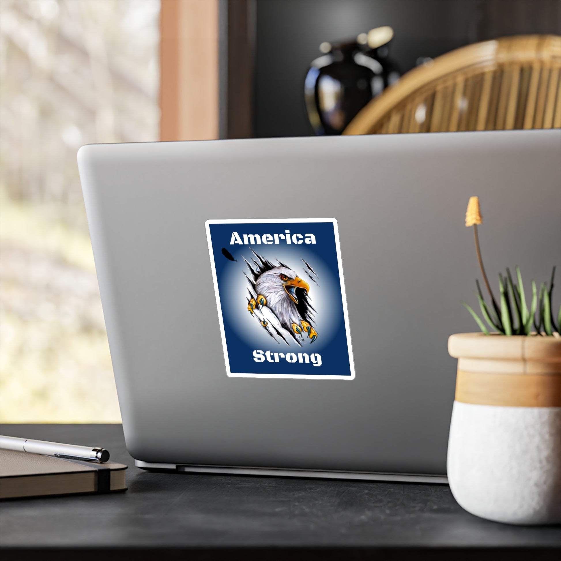 Blue decal showing an eagle ripping through the middle of the design with the words, "America Strong", around the eagle being displayed on the back of a laptop. 